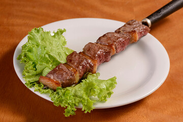 Wall Mural - Meat barbecue on skewers. Traditional Brazilian kebab in white plate on wooden table.