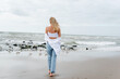© Iaroslava Zolotko - Barefoot blonde woman in a white shirt and blue jeans walking on the beach.