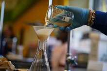Female Hand In A Glove Mixing Chemical Elements And Liquids Through A Filter In Scientific Flasks