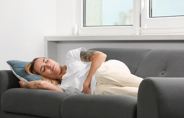 Poster - Young woman suffering from menstrual pain on sofa indoors