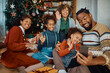 © Drazen - Happy black extended family using mobile phone while greeting someone during video call on Christmas.