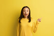 © puhhha - Happy Woman Pointing Aside. Amused Young Girl Points Finger Away at the Empty Copy Space. Pretty Female Isolated on Yellow. Advertising Concept