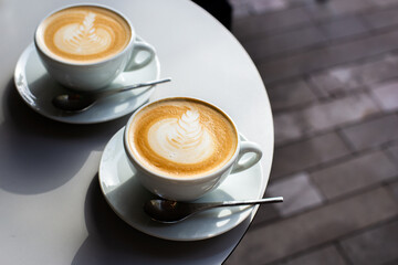 Top view of two hot cappuccino with latte art in white cup and spoon.