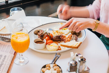 Poster - female hands holding fork and knife while having tasty breakfast at modern european cafe