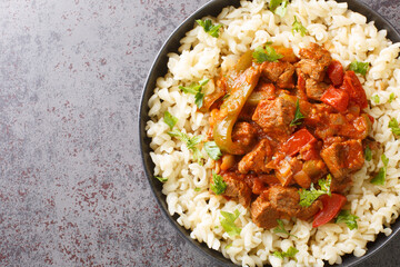 Wall Mural - Porkolt is a Hungarian stew with boneless meat, paprika and some vegetables served with Egg Noodles Nokedli closeup on the plate on the table. Horizontal top view from above