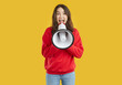 © Studio Romantic - Young brunette woman wearing red sweatshirt is laughing talking in loudspeaker on yellow background. Marketing and sales, announcement and notification, banner for advertising with copy space concept.