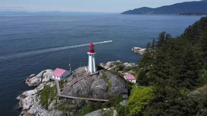 Sticker - Aerial shot of lighthouse at pine forest shore and a boat flushing in the sea in Lighthouse Park