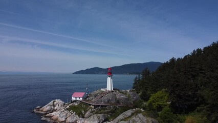 Poster - Aerial shot of lighthouse on a rocky sea shore and mountain pine  forest in Lighthouse Park, Canada