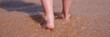 Bare feet of child walking along sea shore closeup
