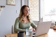© Austockphoto - Woman wearing green sweater with eyeglasses sitting down looking at the laptop on the wooden table