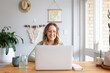 © Austockphoto - Smiling woman working from home on laptop at kitchen table