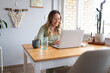 © Austockphoto - Smiling woman working from home on laptop at kitchen table
