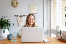 Smiling Woman Working From Home On Laptop At Kitchen Table