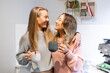 © Austockphoto - Happy female same sex couple standing together, looking at one another with coffees