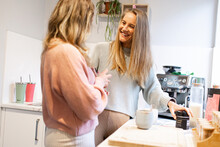 Two Smiling Blonde Women Talking As They Make Coffee In Their  Kitchen