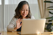 © saltdium - Smiling Old woman chatting on laptop online, sitting at desk in living room.