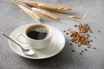 Barley coffee in white cup, beans and ears of barley on gray background. Best natural caffeine free organic coffee alternative. Coffee substitute beverage made of a healthy blend of roasted barley. 