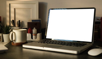 Laptop computer with blank screen, coffee cup and picture frame on black table. Comfortable workplace.