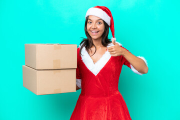 Wall Mural - Young hispanic woman dressed as mama noel holding cartoon box isolated on blue background with thumbs up because something good has happened