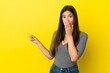 Young Brazilian woman isolated on yellow background with surprise expression while pointing side