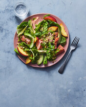 Salad with salmon, peaches, and pistachios on pink plate on blue surface