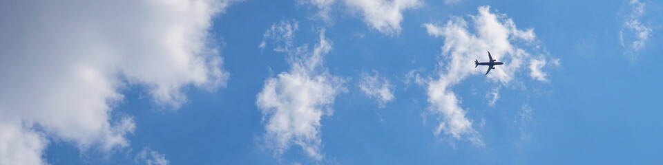 Wall Mural - The passenger airplane is flying far away in the blue sky and white clouds. Plane in the air. International passenger air transportation. The airplane flies in the distance. Banner or header
