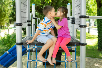 Children play on the outdoor playground. Children's love. A boy and a girl are kissing.