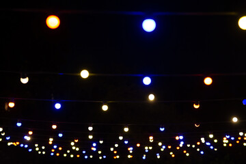 Wall Mural - A view from below of a lot of small light bulbs, a festive garland illuminating the night sky.