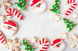 © Jenifoto - Cute Christmas cookie frame. Top down view on a white marble background with copy space. Holiday baking concept. Santa Claus, tree, snowflakes, candy canes, stars.
