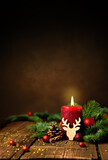 Fototapeta Kosmos - Kerze zum 1. Advent und Weihnachten. Dekoration mit roter Adventskerze, Tannenzweigen, Zapfen, Kugeln und Rentier auf Holz. Hochformat mit Textraum