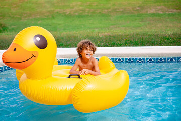 Smiling African American little boy playing in the swimming pool with a large inflatable duck. Having fun in the sun and water