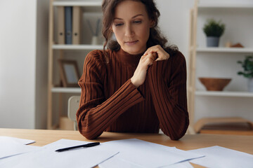 Pensive pondering unhappy sad curly beautiful woman lost in heavy thoughts looks down think about difficult life decision sitting at home office. People problems concept