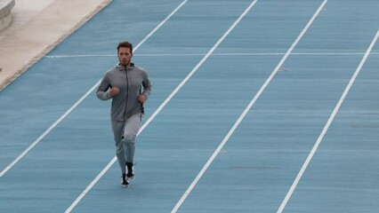 Wall Mural - Runner. Running man training on athletics track and field stadium. Male athlete runner in jogging warming up in sweatsuit. Run sport concept. Slow motion shot at 59.94 FPS