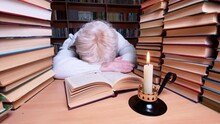 Sad Woman Using Candle Reading Book In Library. Energy Crisis Concept. Lack Of Heating And Electric Lighting. 