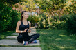 © VK Studio - Cheerful female runner poses in lotus pose outdoor dressed in sportswear uses mobile phone during rest after jog downloads music songs in player prepares for morning workout chooses audio records
