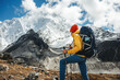 © leonidkos - Solo tourist with travel backpack stand in front of snowy and cloudy mountains. Traveler among high altitude mountain