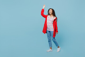 Poster - Full body smiling happy fun young woman of African American ethnicity 20s she wear red jacket walk go waving hand isolated on plain pastel light blue cyan background. Wet fall weather season concept.