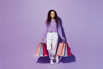 Full body happy smiling young woman 20s wears pullover hold in hand paper package bags after shopping look camera isolated on plain pastel light purple background. Black Friday sale buy day concept.