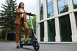 Businesswoman with modern electric kick scooter on city street, low angle view. Space for text