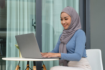 Wall Mural - Portrait of Muslim asian woman in hijab using laptop at home.