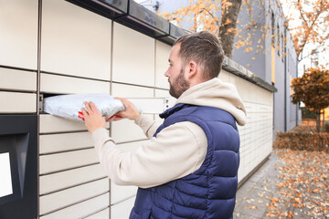 Happy bearded man put the parcel in the self-service mail terminal. Parcel delivery machine.