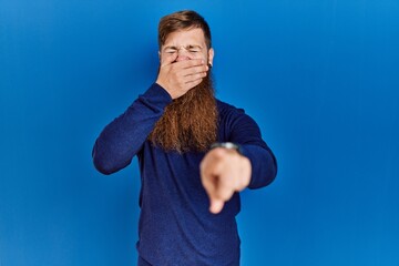 Canvas Print - Redhead man with long beard wearing casual blue sweater over blue background laughing at you, pointing finger to the camera with hand over mouth, shame expression