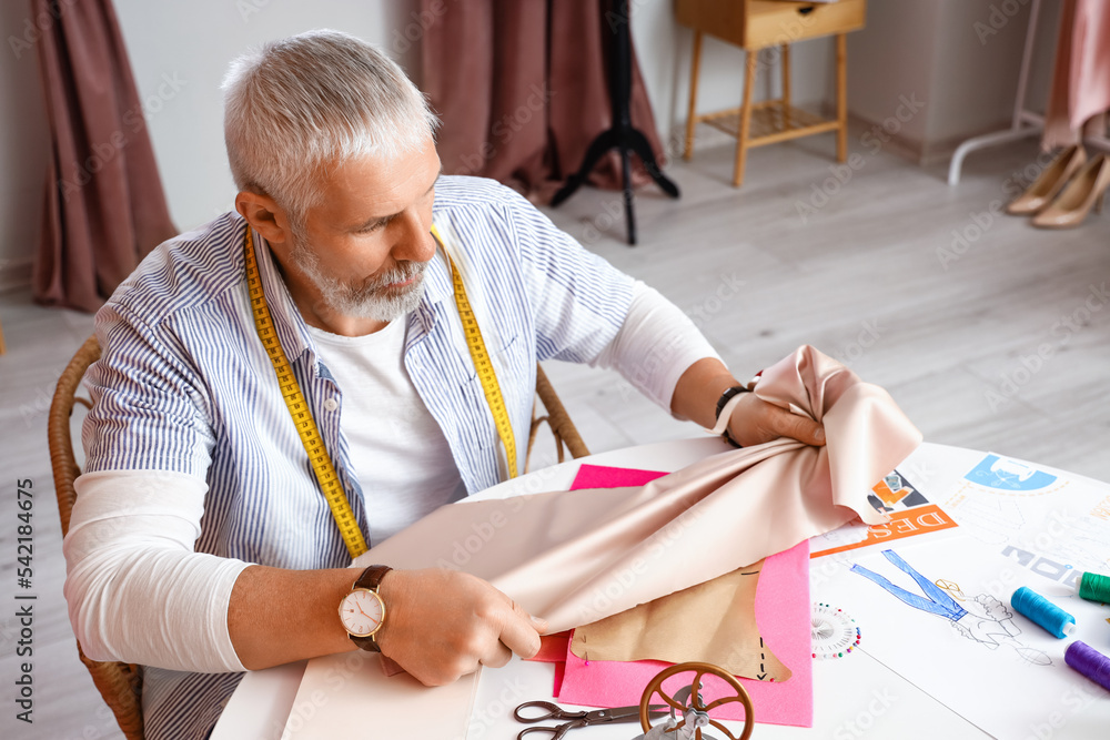 Mature fashion designer working with fabric at table in studio