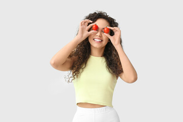 Poster - Funny young African-American woman with cherry tomatoes on light background. Diet concept