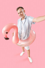 Canvas Print - Young man with inflatable ring taking selfie on pink background