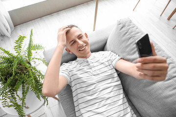 Canvas Print - Young man with mobile phone taking selfie on sofa at home