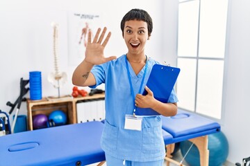 Poster - Young hispanic woman with short hair working at pain recovery clinic doing stop gesture with hands palms, angry and frustration expression