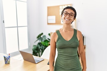 Canvas Print - Young hispanic woman with short hair working at the office looking positive and happy standing and smiling with a confident smile showing teeth