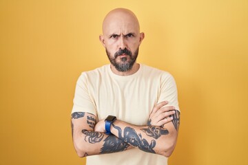 Poster - Hispanic man with tattoos standing over yellow background skeptic and nervous, disapproving expression on face with crossed arms. negative person.