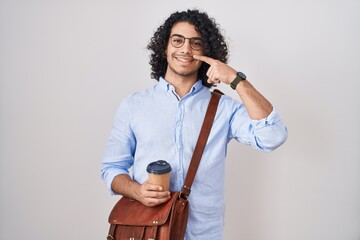 Wall Mural - Hispanic man with curly hair drinking a cup of take away coffee pointing with hand finger to face and nose, smiling cheerful. beauty concept